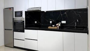 Eine Küche mit weißen Schränken, einer schwarzen Arbeitsplatte, einem eingebauten Backofen, einer Mikrowelle und einem Edelstahl-Kühlschrank.