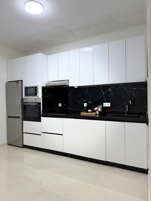 A kitchen with white cabinets, a black countertop, a built-in oven, a microwave, and a stainless steel refrigerator. - 3-bedroom apartment in peaceful Tangier (Tangier)
