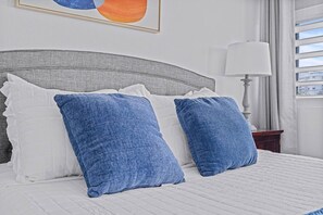 Ein Bett mit grauem Kopfteil, weißer Bettwäsche und zwei blauen Kissen.