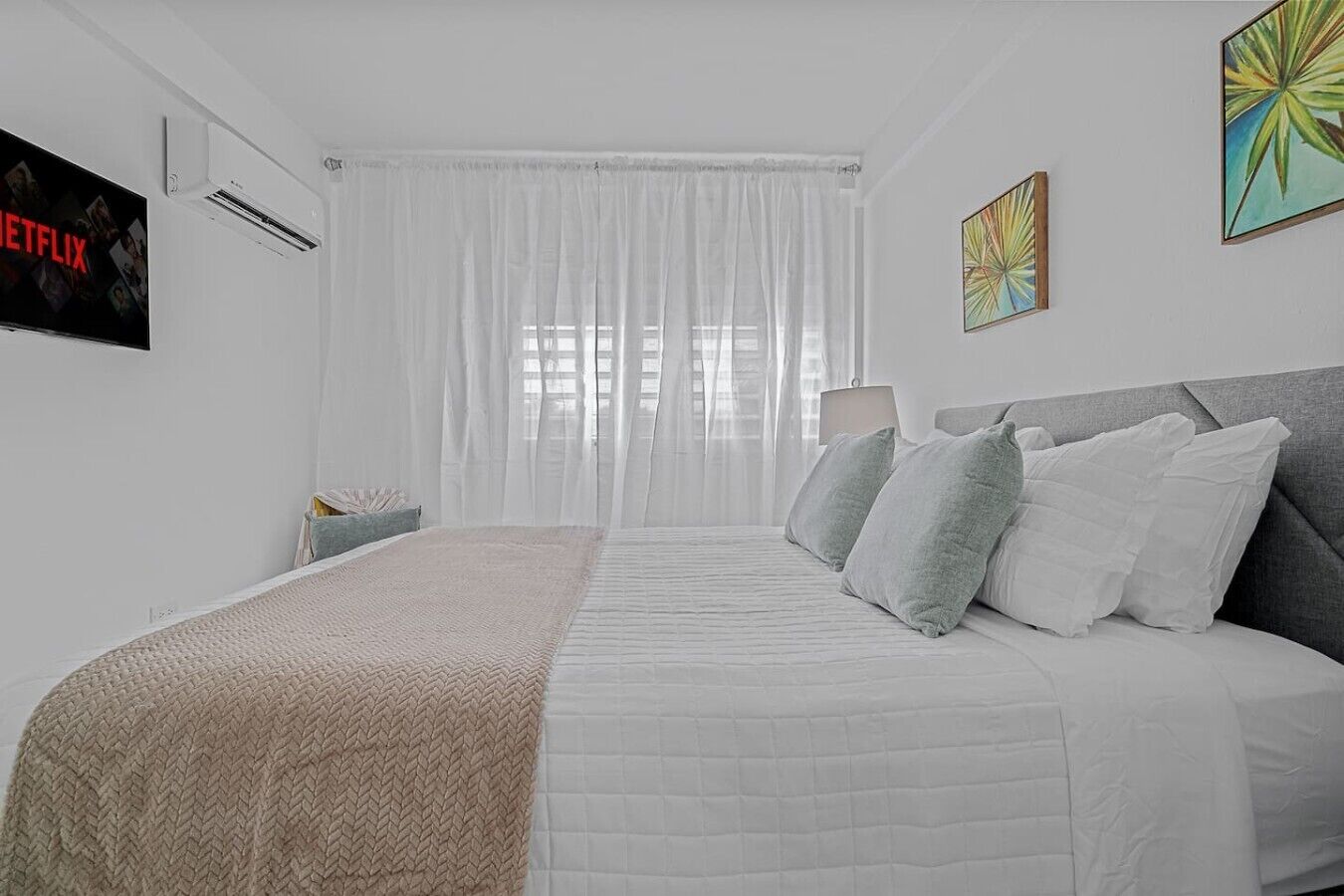 A modern hotel room with a large bed, a TV, and artwork on the walls.