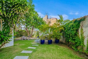 A garden with potted plants, a pathway, and a building in the background. - Ocean Park 2BR · Steps to Beach & Dining (San Juan)