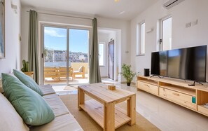 A modern living room with a sofa, a wooden coffee table, a TV, and a balcony with a view of buildings. - Charming bright penthouse with 3 Terraces JCUT2-1 (Swieqi)