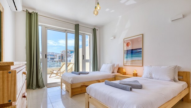 A hotel room with two wooden beds, a large window with curtains, a chair outside, and a painting on the wall. - Charming bright penthouse with 3 Terraces JCUT2-1 (Swieqi)