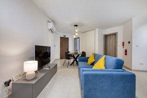 Ein modernes Wohnzimmer mit einer Couch, einem Fernseher und einem Essbereich im Hintergrund.