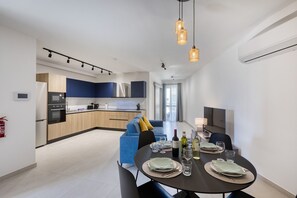 Eine moderne Küche mit Einbaugeräten, ein Essbereich mit rundem Tisch für vier Personen und ein Wohnbereich mit Sofa und Fernseher.