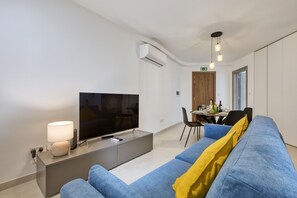 Ein modernes Wohnzimmer mit Flachbildfernseher, einer Couch, einem Essbereich und einer Klimaanlage.