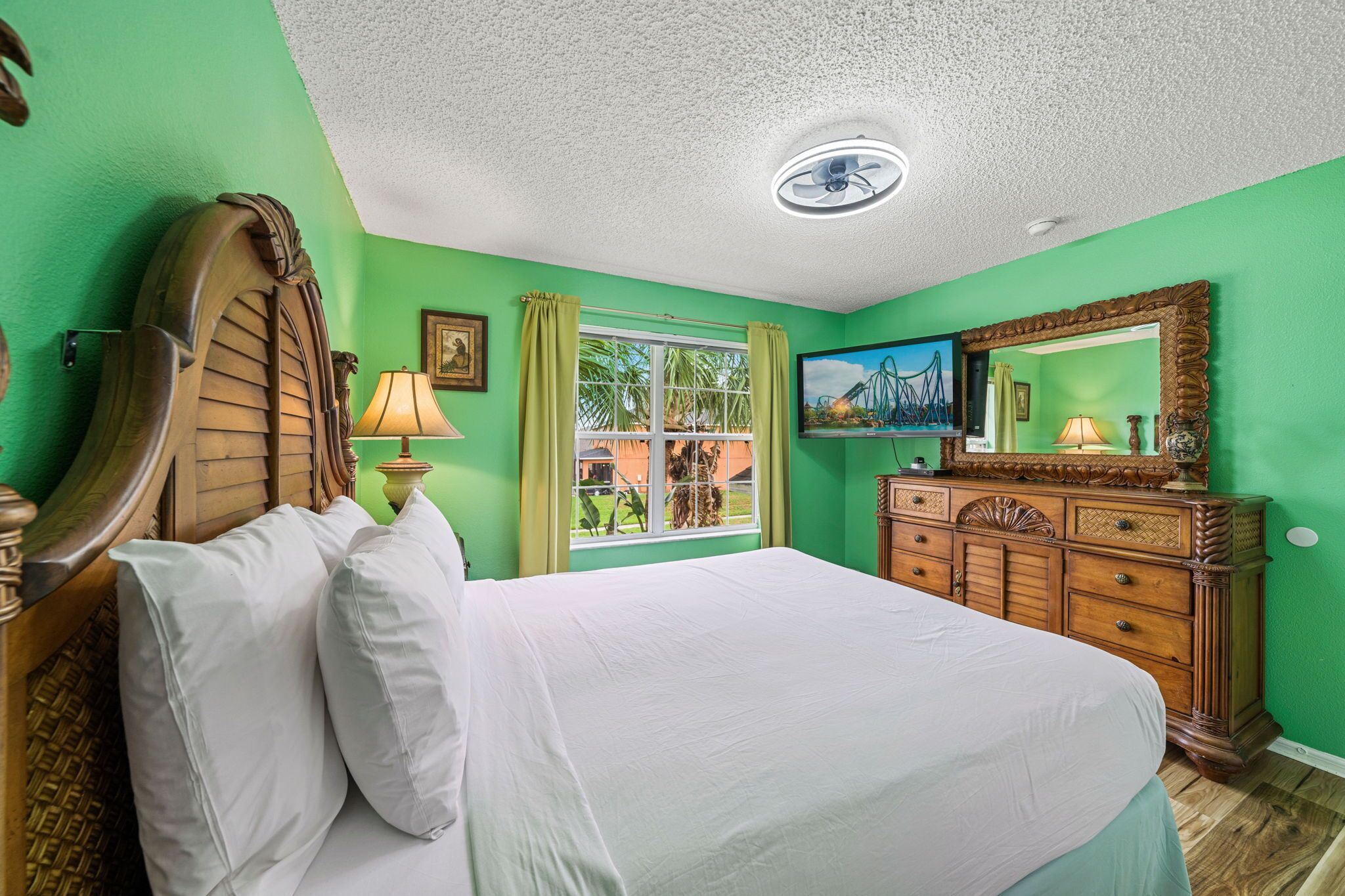 Une chambre à coucher avec un lit, une commode, un téléviseur et une fenêtre avec des rideaux.