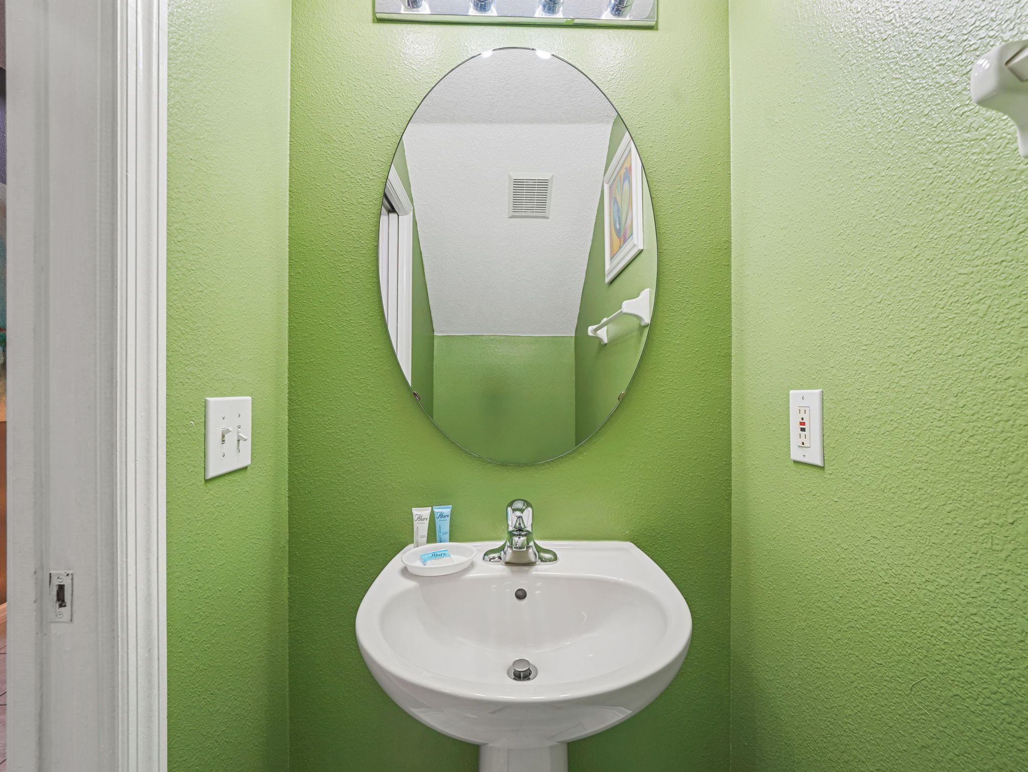 A bathroom with a green wall, a white sink, a mirror, and a hand dryer.