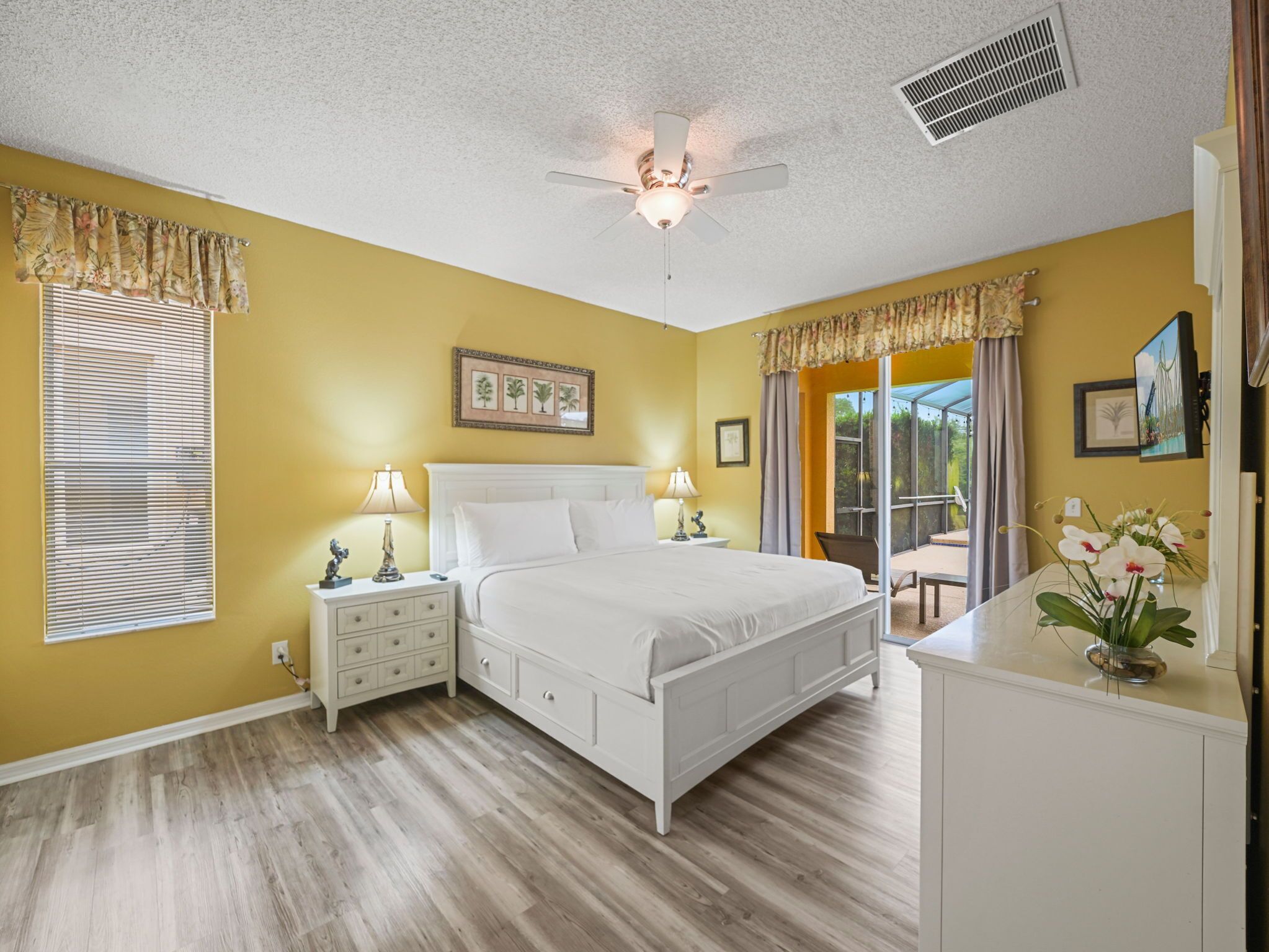 A bedroom with a bed, bedside tables, a ceiling fan, and a view to the outside.