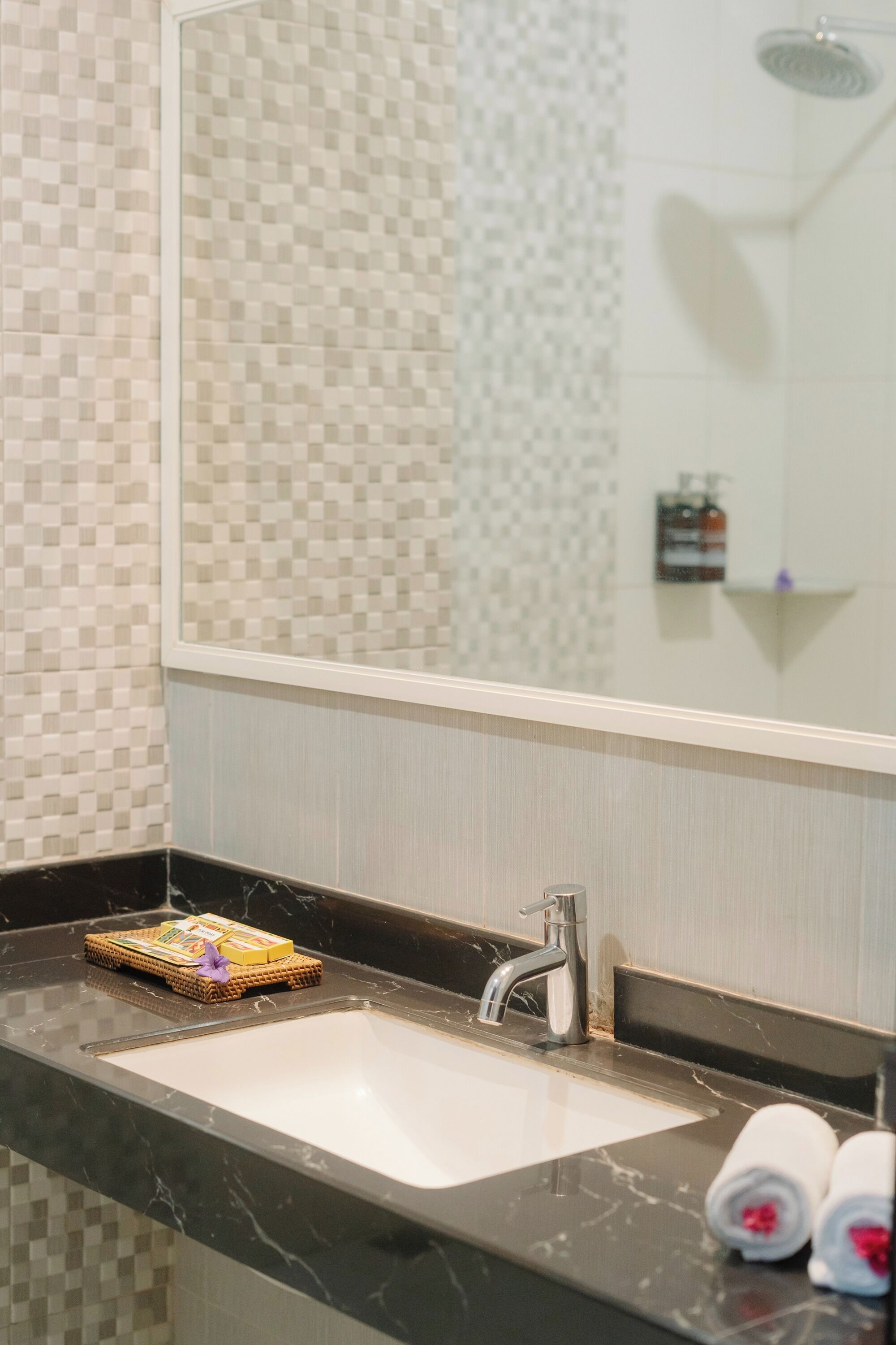 Une salle de bain avec un mur recouvert de carreaux à motifs, un miroir, un lavabo avec un plan de travail en marbre et un espace douche.