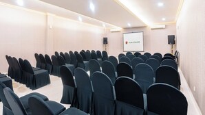 Uma sala de conferências com fileiras de cadeiras, uma tela de projetor e alto-falantes.