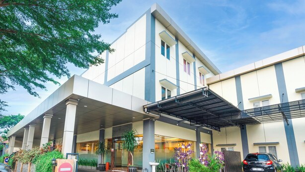 Entrada moderna de hotel com área de espera coberta, mobiliário para área externa e estacionamento.