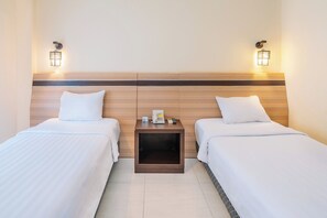 Habitació d'hotel amb dos llits, un capçal de llit de fusta, làmpades a cada costat del llit i una taula petita amb un telèfon i un comandament.