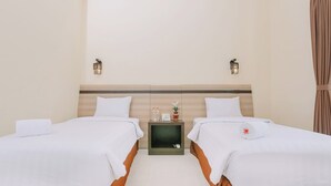 Quarto de hotel com duas camas, uma mesa de cabeceira, um abajur e uma cortina.