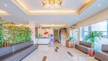 A hotel lobby with a reception desk, seating areas, a staircase, and a large window.