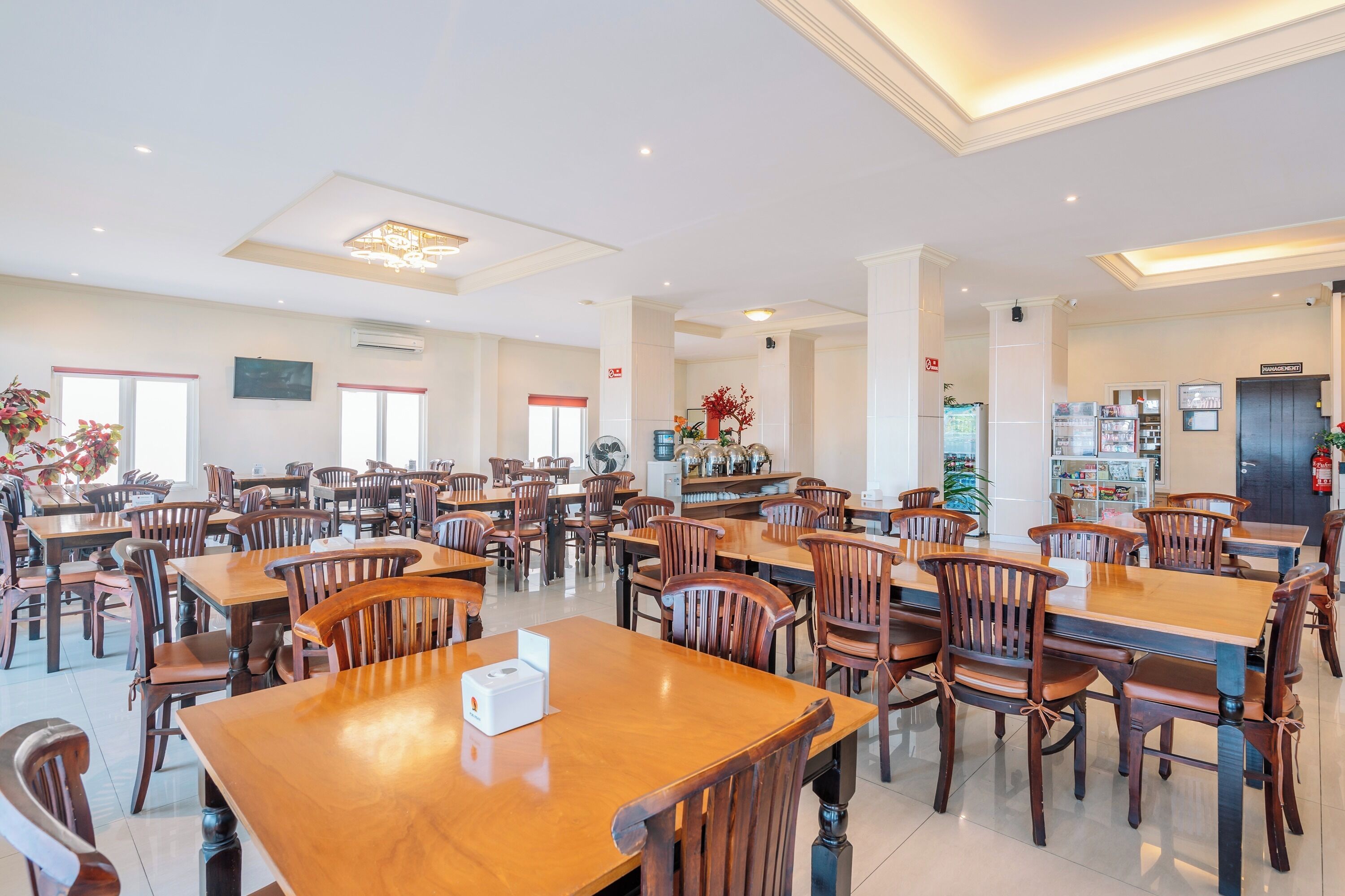 Un comedor amplio con varias mesas y sillas de madera, una zona de bar y un ventanal que proporciona luz natural.