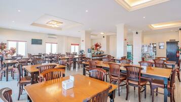 Un comedor amplio con varias mesas y sillas de madera, una zona de bar y un ventanal que proporciona luz natural.