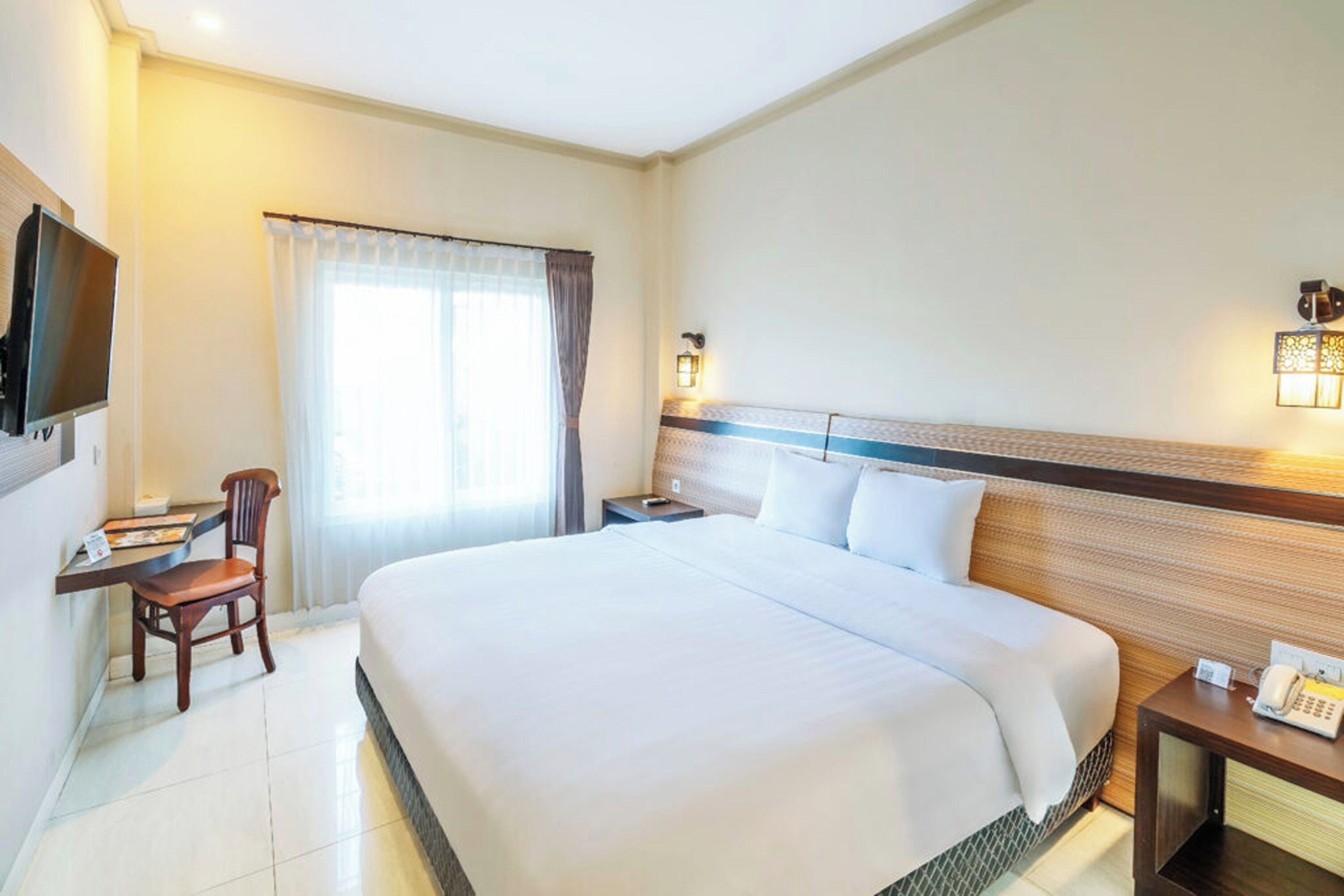 Habitació d'hotel amb un llit gran, un escriptori amb cadira, una televisió i una taula de nit amb telèfon.