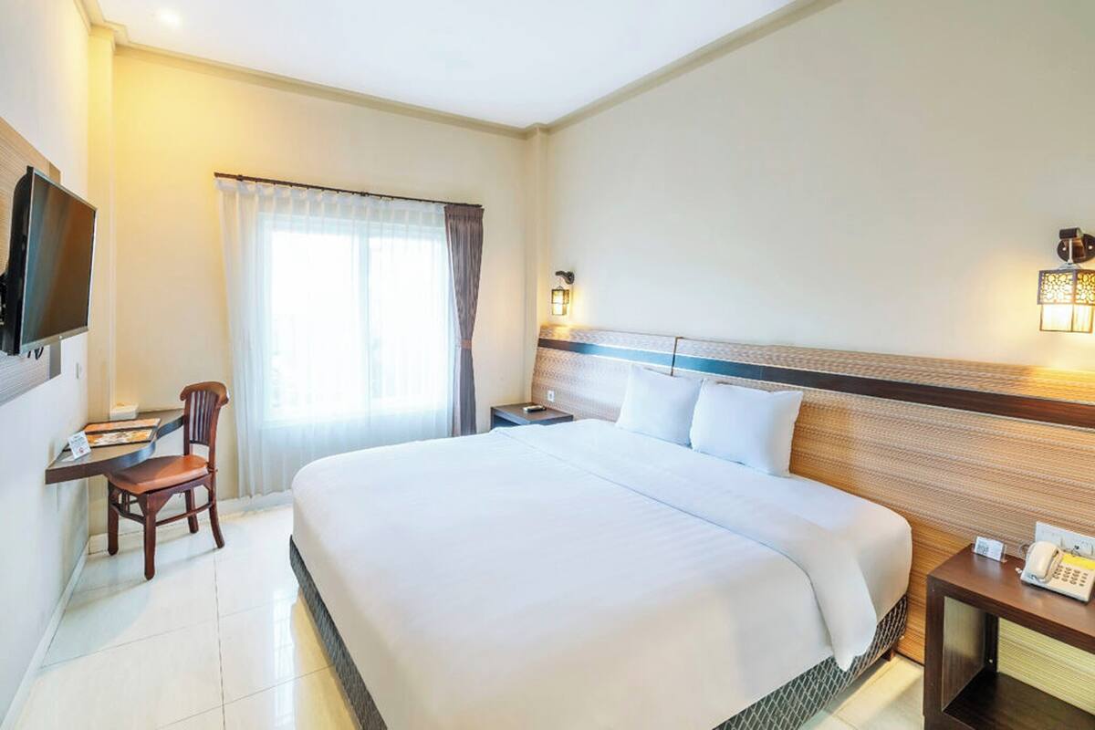 A hotel room with a large bed, a desk with a chair, a TV, and a bedside table with a phone.