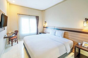 A hotel room with a large bed, a desk with a chair, a TV, and a bedside table with a phone. - Hotel Puri Indah Subak (Mataram)