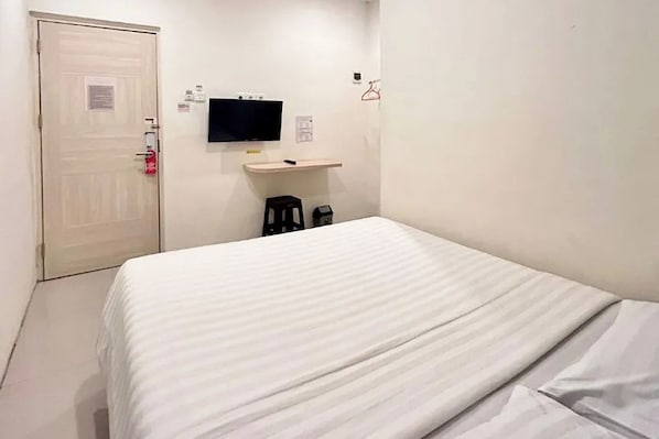 Habitación de hotel con cama, televisor montado en la pared, un taburete pequeño y una puerta con detector de incendios.