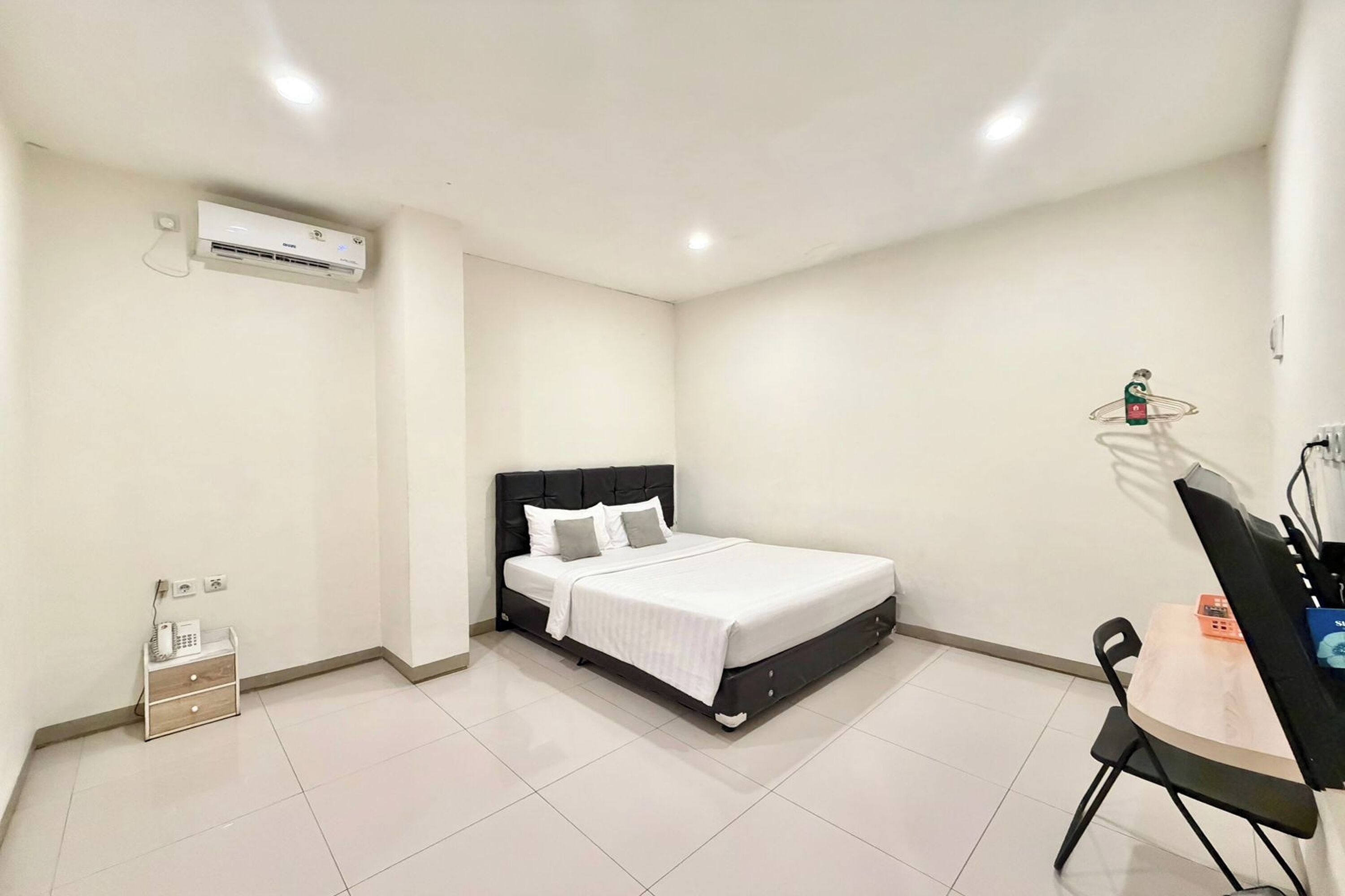 A bedroom with a bed, bedside table, chair, and an air conditioning unit.