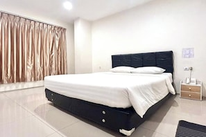 Una habitación de hotel con cama, mesita de noche, teléfono y ventana con cortinas.