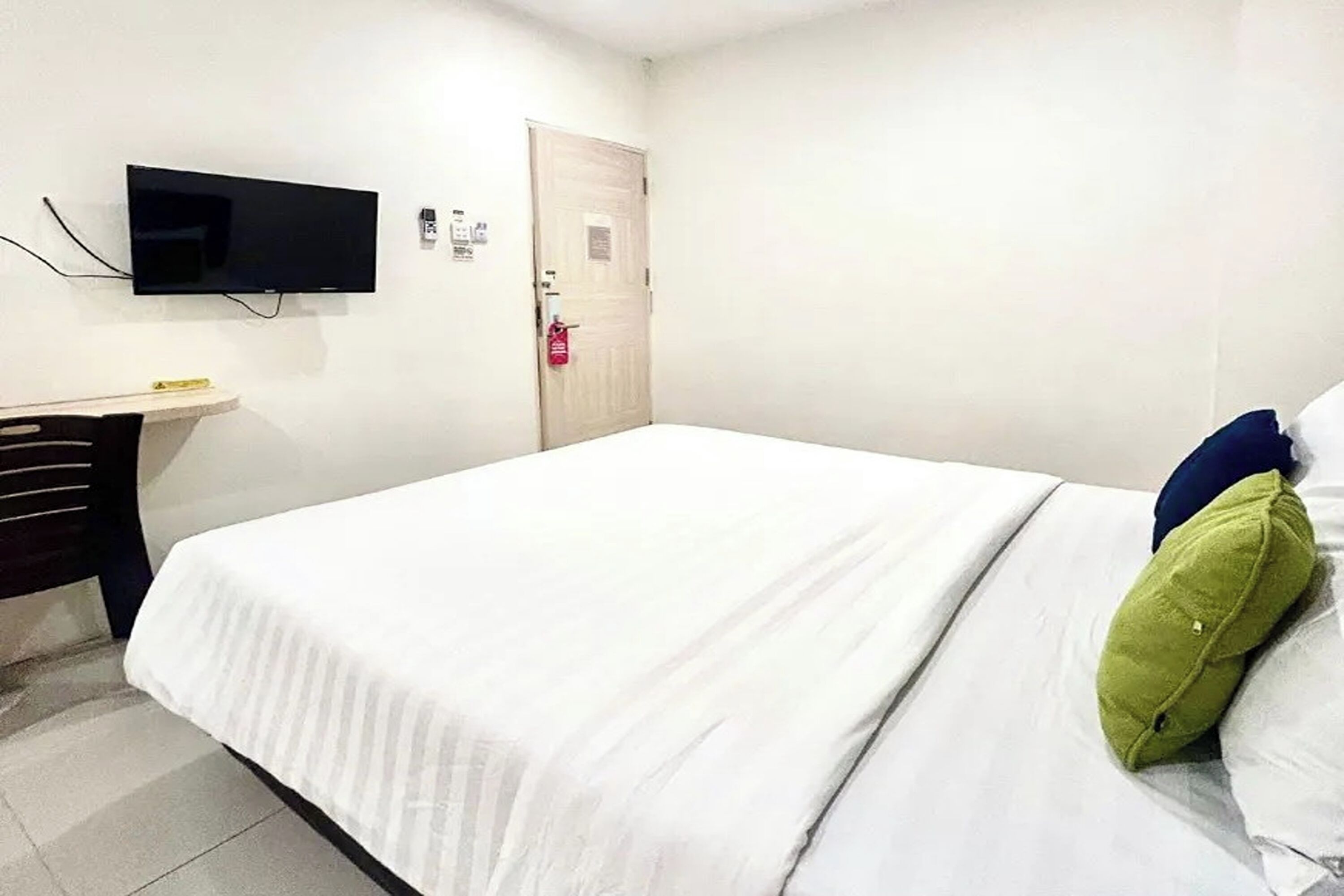 Habitación de hotel con cama, un televisor de pantalla plana montado en la pared, un escritorio y una puerta con detector de incendios.