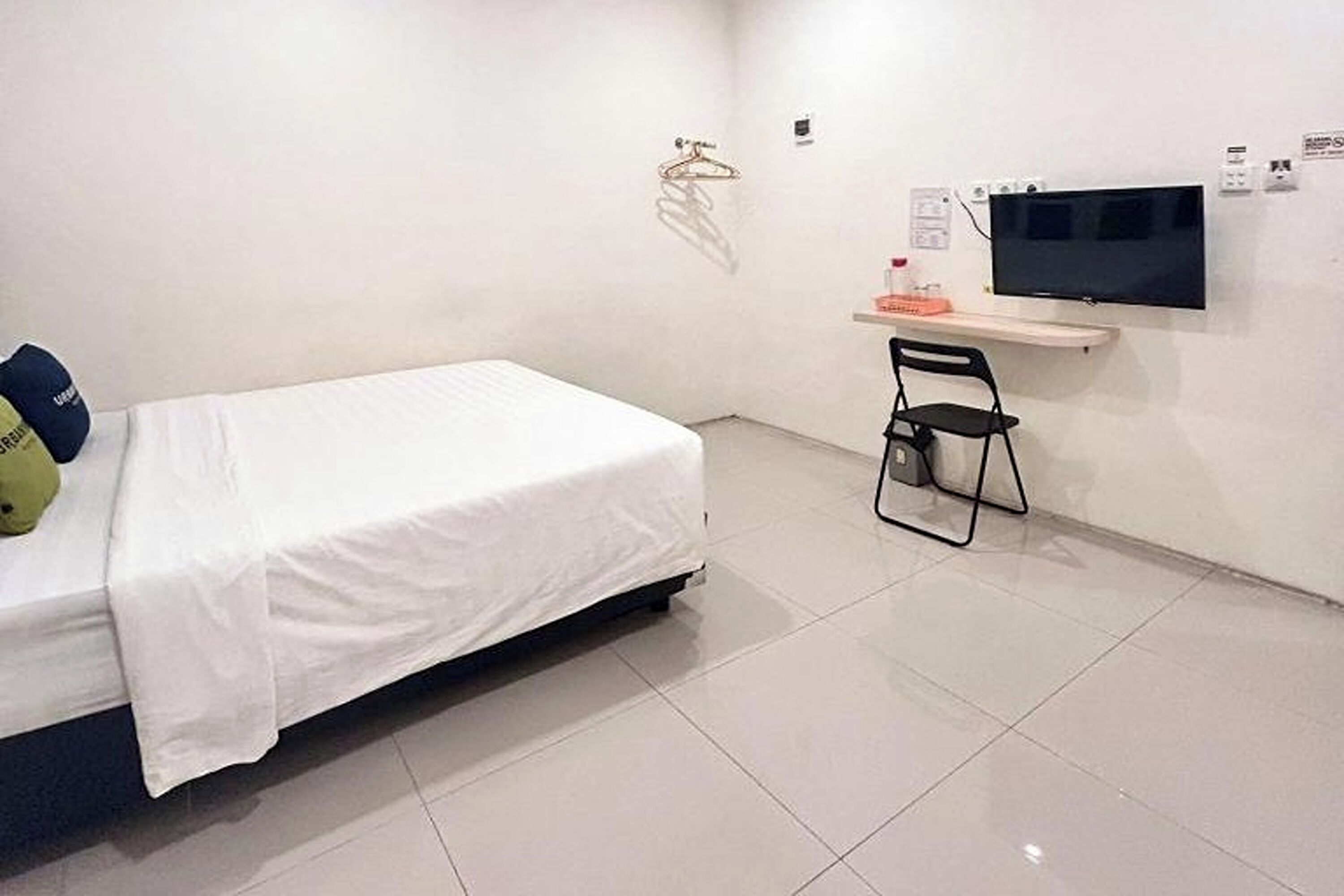 A room with a bed, a chair, a TV mounted on the wall, and a small shelf with items.