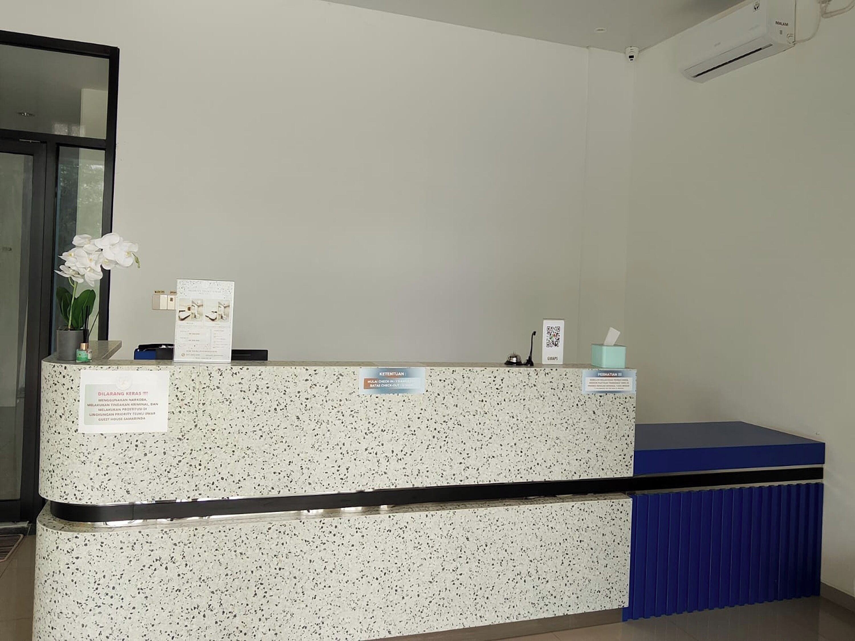 A reception desk with a sign, a potted plant, and a tissue box.