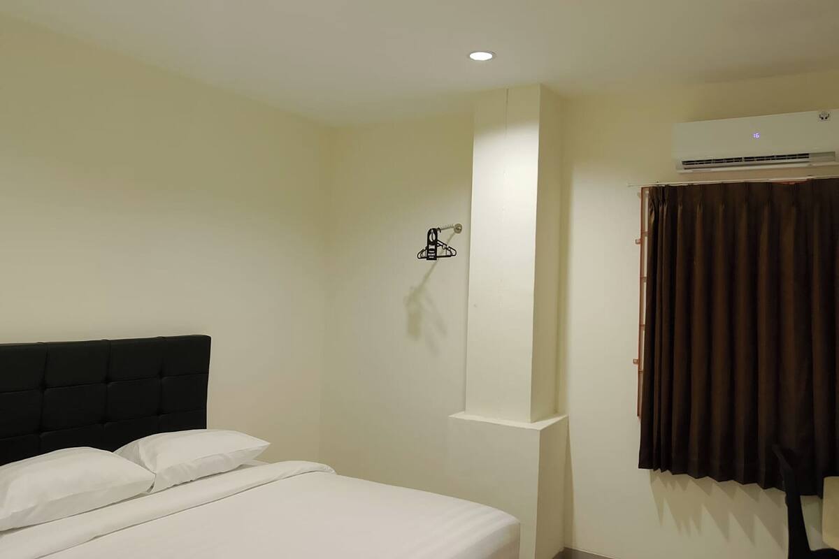 A hotel room with a bed, a wall-mounted air conditioning unit, and a window with curtains.