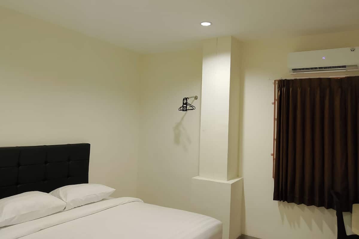 Una habitación de hotel con una cama, un aire acondicionado de pared y una ventana con cortinas.