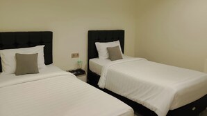 A room with two beds, each with a black headboard and white bedding. There is a nightstand with a lamp and a bottle on it. - Priority Teuku Umar Samarinda (Samarinda)
