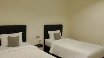 A room with two beds, each with a black headboard and white bedding. There is a nightstand with a lamp and a bottle on it.