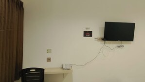 A room with a flat-screen TV mounted on the wall, a desk with a telephone, and an air conditioning unit above the desk. - Priority Teuku Umar Samarinda (Samarinda)
