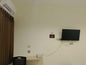 Una habitación con televisión de pantalla plana montada en la pared, un escritorio con teléfono y un equipo de aire acondicionado sobre el escritorio.