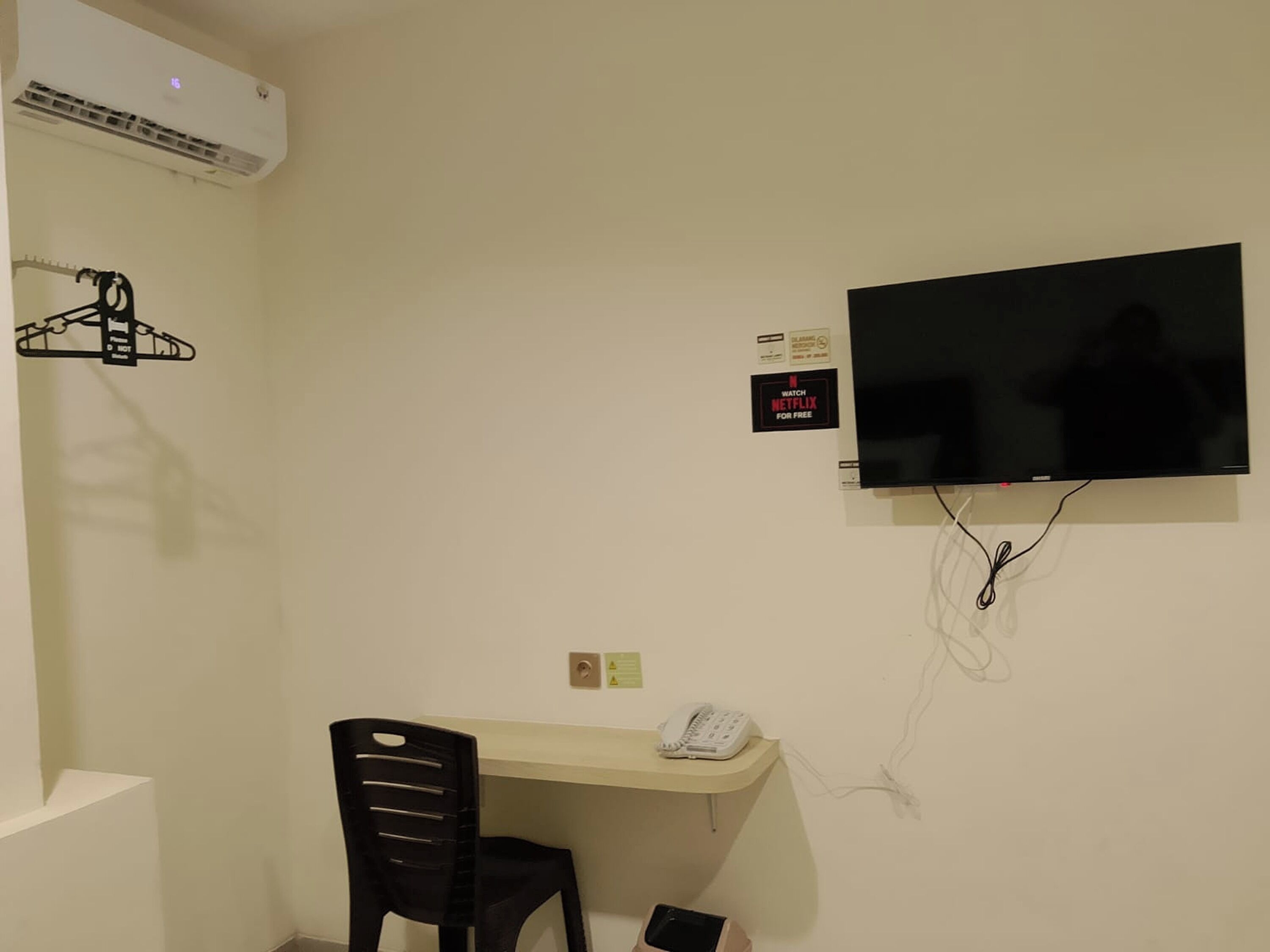 Una habitación con escritorio, una silla, televisor montado en la pared, teléfono y aire acondicionado instalado.