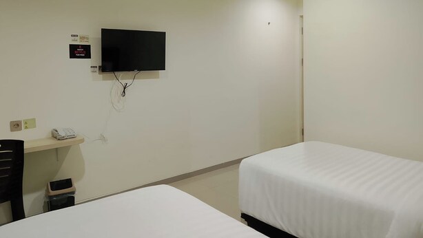 A hotel room with a flat-screen TV mounted on the wall, a desk with a telephone, and two single beds. - Priority Teuku Umar Samarinda (Samarinda)