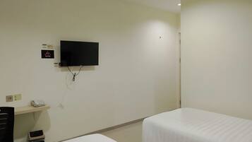 Ein Hotelzimmer mit einem an der Wand befestigten Flachbildfernseher, einem Schreibtisch mit Telefon und zwei Einzelbetten.