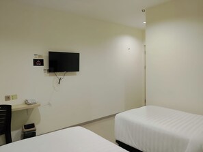 A hotel room with a flat-screen TV mounted on the wall, a desk with a telephone, and two single beds. - Priority Teuku Umar Samarinda (Samarinda)