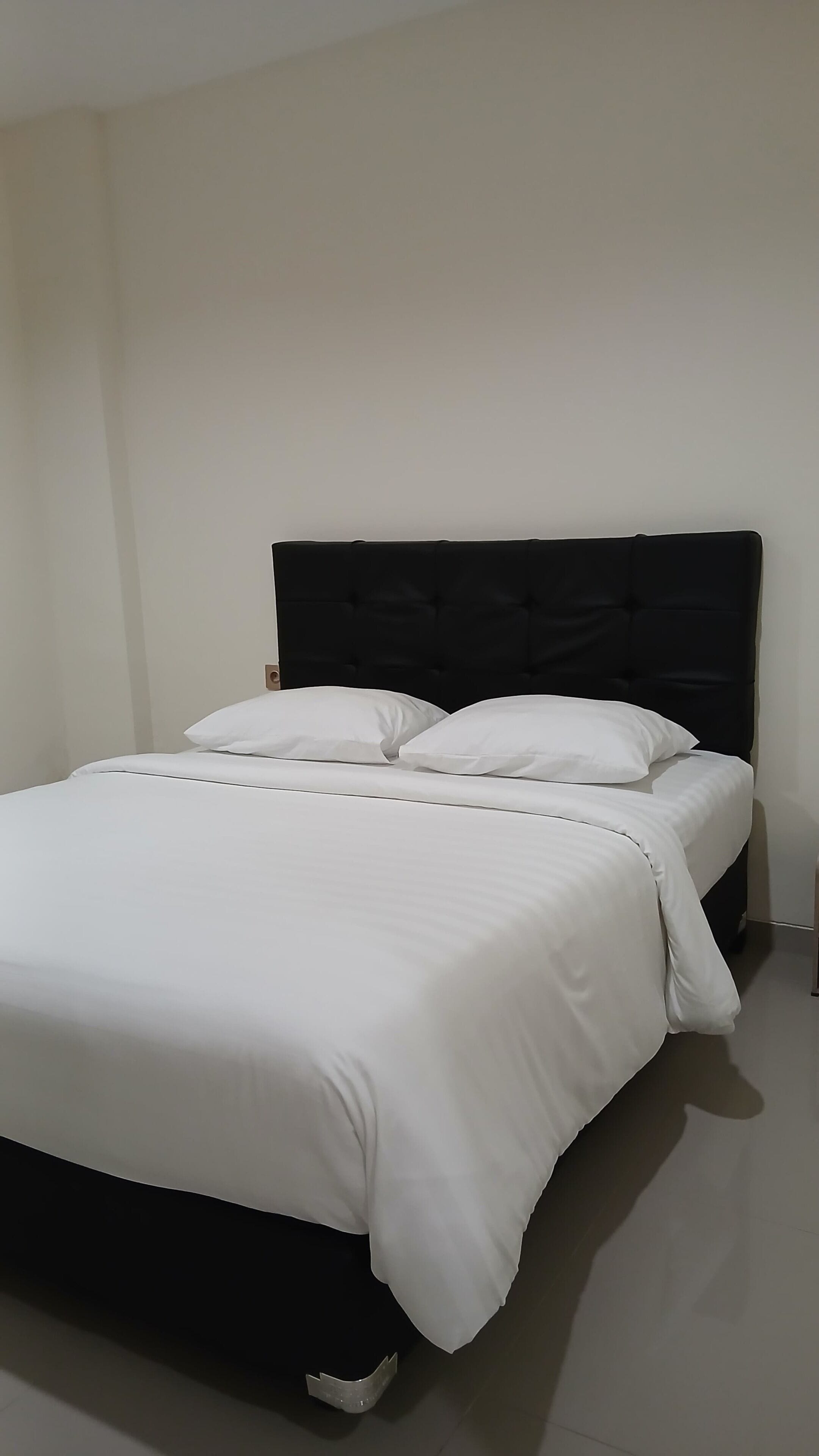 A bed with a black headboard and white bedding in a room with plain walls.
