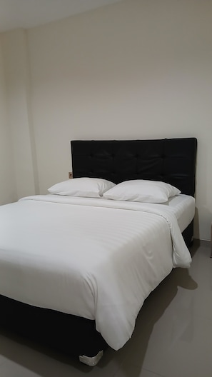 A bed with a black headboard and white bedding in a room with plain walls. - Priority Teuku Umar Samarinda (Samarinda)
