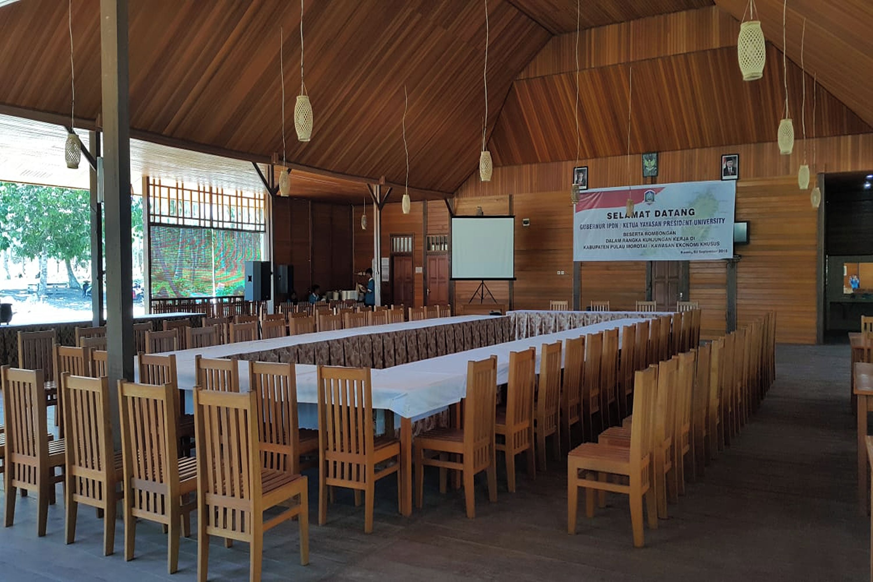 A conference room with a long table and chairs, a projection screen, and a banner on the wall.
