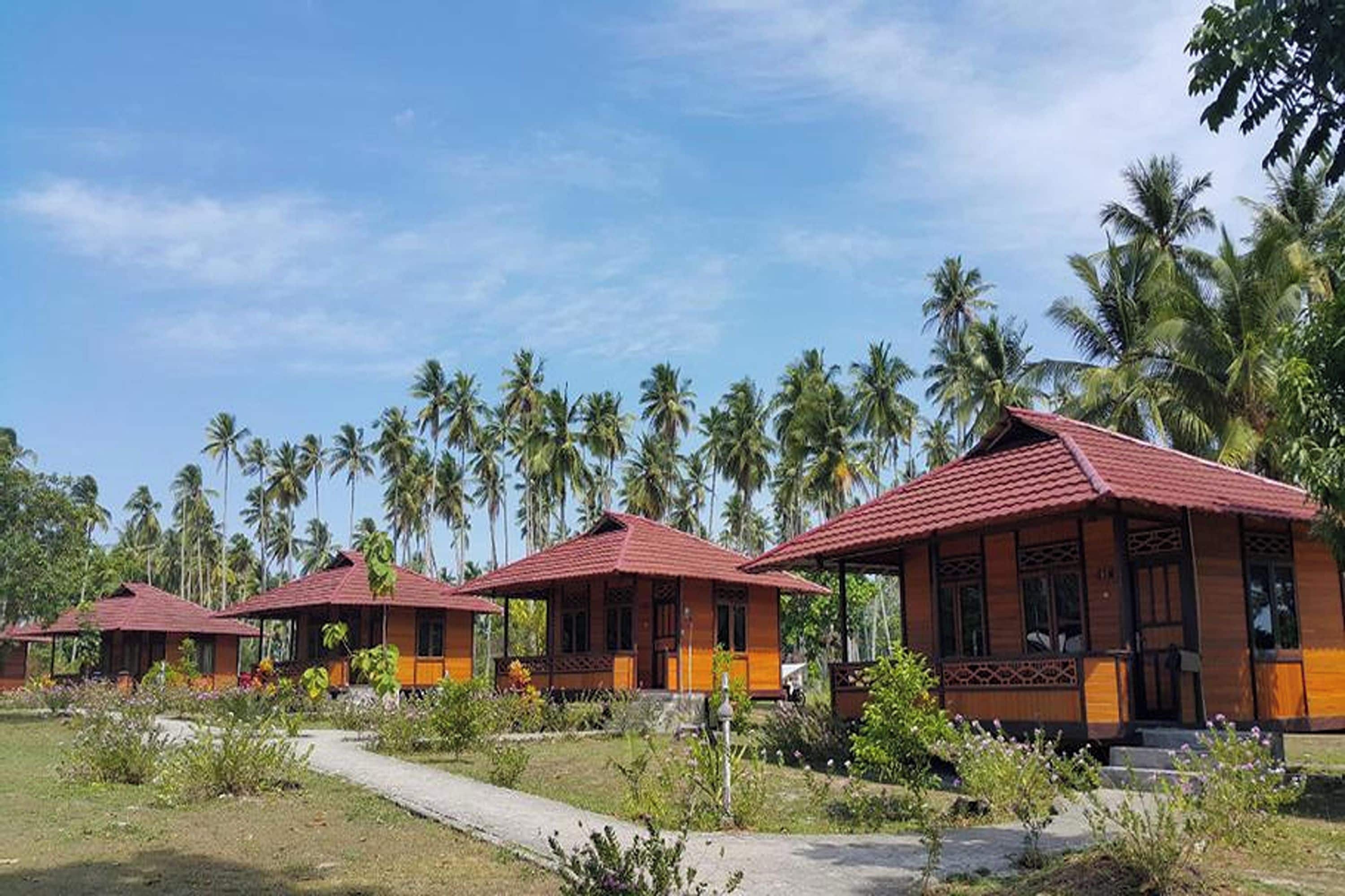 A row of traditional-style buildings with red roofs, surrounded by lush greenery and palm trees.