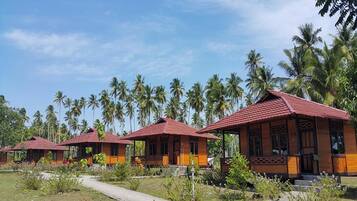 A row of traditional-style buildings with red roofs, surrounded by lush greenery and palm trees.