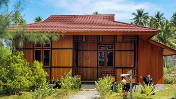 A wooden house with a tiled roof, surrounded by greenery and palm trees.