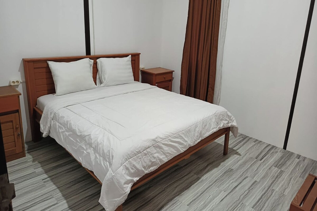 Une chambre d’hôtel standard avec un cadre de lit en bois, du linge de lit blanc et une petite table de chevet.