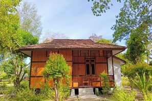 Une maison traditionnelle en bois, avec un toit recouvert de tuiles, entourée d’une végétation luxuriante.