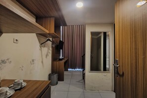 A compact hotel room with a wooden desk, a small trash bin, and a door leading to another room.