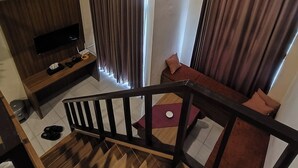 Una sala de estar moderna con un televisor de pantalla plana, un mueble de madera para entretenimiento, una escalera y un sofá con cojines.